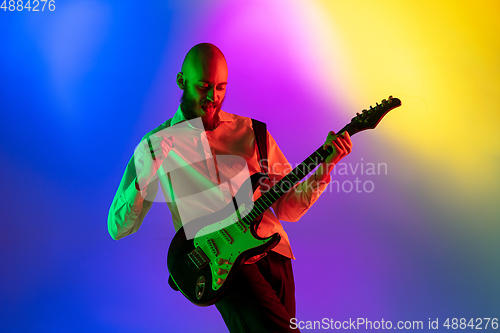 Image of Young caucasian musician, guitarist playing on gradient background in neon light. Concept of music, hobby, festival