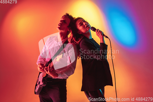 Image of Young caucasian musicians, female singer and guitarist performing on gradient background in neon light. Concept of music, hobby, festival