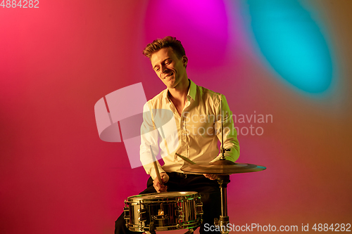 Image of Young caucasian musician, drummer playing on gradient background in neon light. Concept of music, hobby, festival