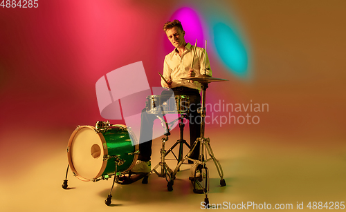 Image of Young caucasian musician, drummer playing on gradient background in neon light. Concept of music, hobby, festival