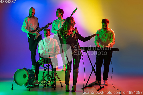 Image of Young caucasian musicians, band playing on gradient background in neon light. Concept of music, hobby, festival
