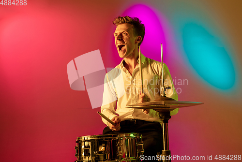 Image of Young caucasian musician, drummer playing on gradient background in neon light. Concept of music, hobby, festival