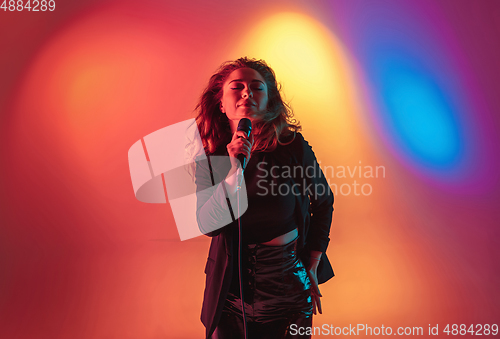 Image of Young caucasian musician, female singer performing on gradient background in neon light. Concept of music, hobby, festival