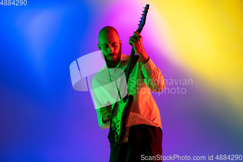 Image of Young caucasian musician, guitarist playing on gradient background in neon light. Concept of music, hobby, festival