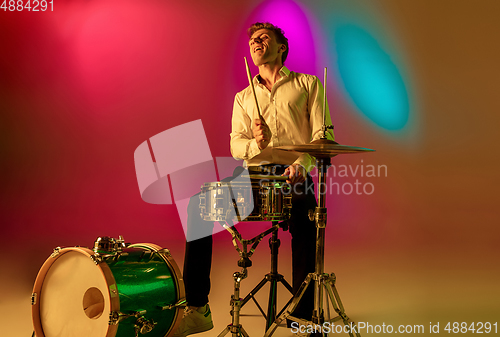 Image of Young caucasian musician, drummer playing on gradient background in neon light. Concept of music, hobby, festival