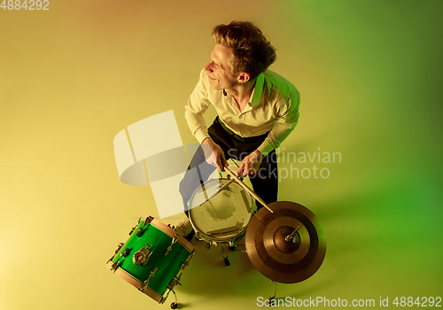 Image of Young caucasian musician, drummer playing on gradient background in neon light. Concept of music, hobby, festival