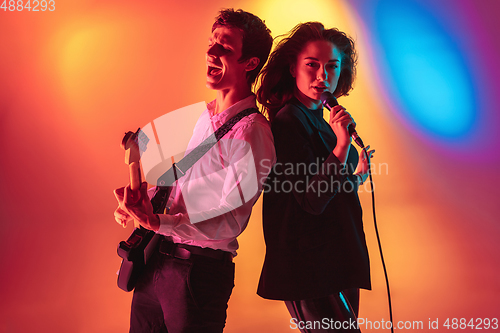 Image of Young caucasian musicians, female singer and guitarist performing on gradient background in neon light. Concept of music, hobby, festival