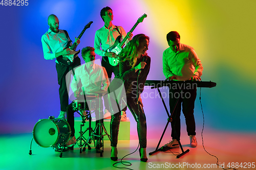 Image of Young caucasian musicians, band playing on gradient background in neon light. Concept of music, hobby, festival