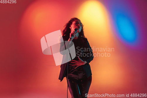Image of Young caucasian musician, female singer performing on gradient background in neon light. Concept of music, hobby, festival