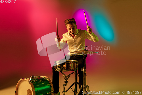 Image of Young caucasian musician, drummer playing on gradient background in neon light. Concept of music, hobby, festival