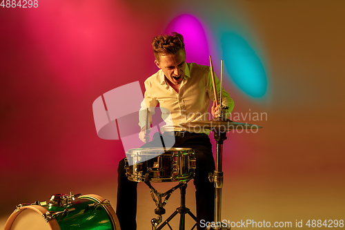 Image of Young caucasian musician, drummer playing on gradient background in neon light. Concept of music, hobby, festival