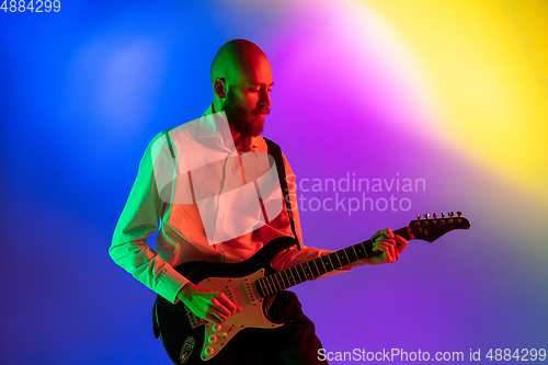 Image of Young caucasian musician, guitarist playing on gradient background in neon light. Concept of music, hobby, festival