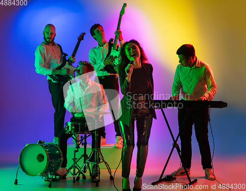 Image of Young caucasian musicians, band playing on gradient background in neon light. Concept of music, hobby, festival