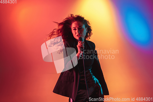 Image of Young caucasian musician, female singer performing on gradient background in neon light. Concept of music, hobby, festival