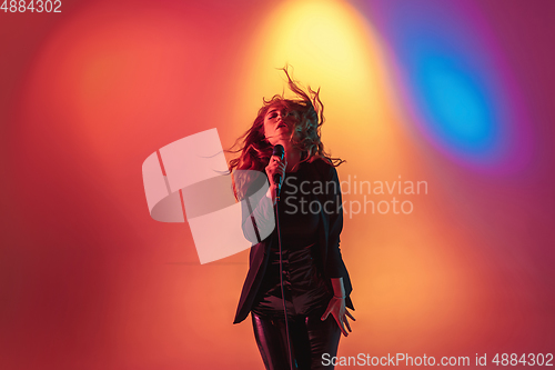 Image of Young caucasian musician, female singer performing on gradient background in neon light. Concept of music, hobby, festival