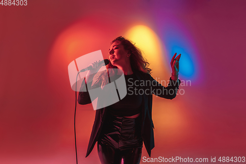 Image of Young caucasian musician, female singer performing on gradient background in neon light. Concept of music, hobby, festival