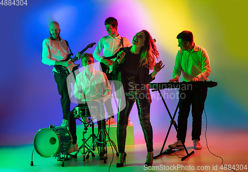 Image of Young caucasian musicians, band playing on gradient background in neon light. Concept of music, hobby, festival