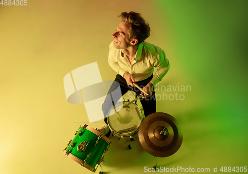 Image of Young caucasian musician, drummer playing on gradient background in neon light. Concept of music, hobby, festival