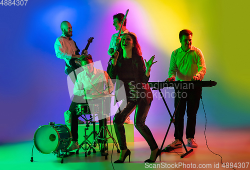 Image of Young caucasian musicians, band playing on gradient background in neon light. Concept of music, hobby, festival