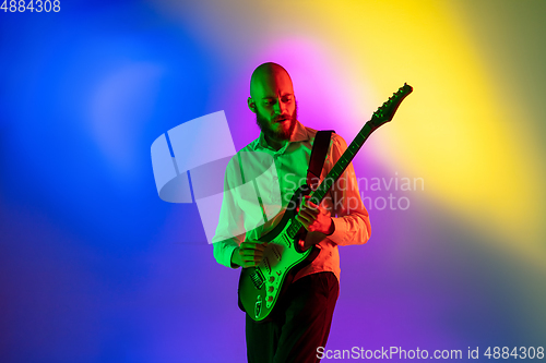 Image of Young caucasian musician, guitarist playing on gradient background in neon light. Concept of music, hobby, festival