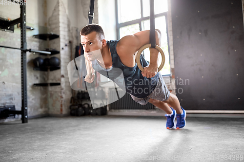 Image of man doing push-ups on gymnastic rings in gym