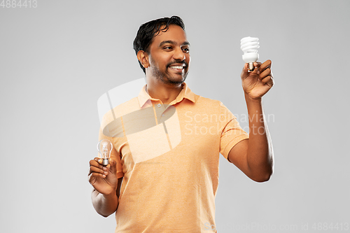 Image of smiling indian man comparing different light bulbs