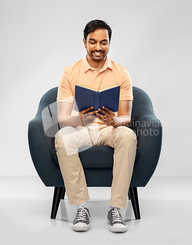 Image of happy young indian man reading book in chair