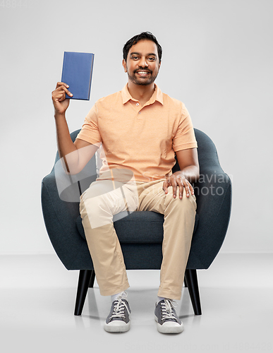 Image of happy young indian man showing book in chair