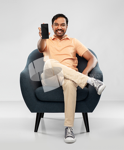 Image of happy young indian man showing smartphone in chair