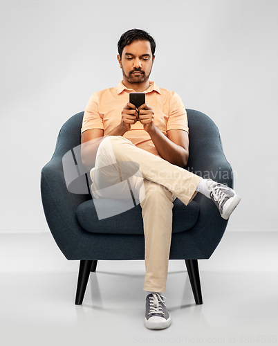 Image of young indian man with smartphone in chair