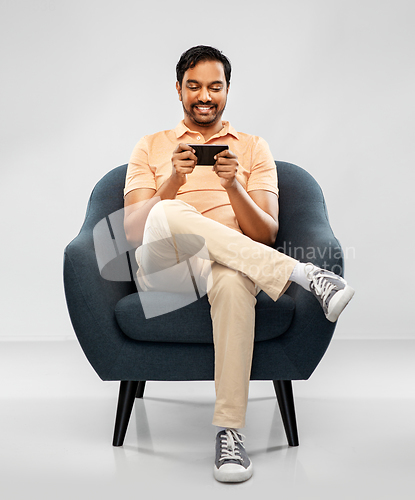 Image of happy young indian man with smartphone in chair