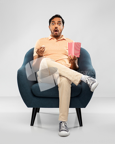 Image of shocked indian man eating popcorn in chair