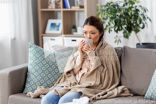 Image of sad sick asian woman drinking hot tea at home