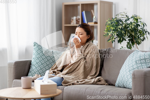 Image of sick asian woman blowing nose with tissue at home