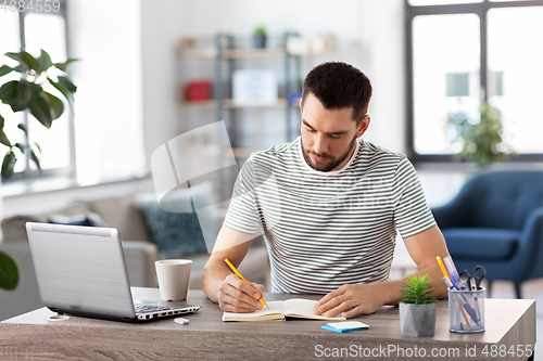 Image of man with notebook and laptop at home office