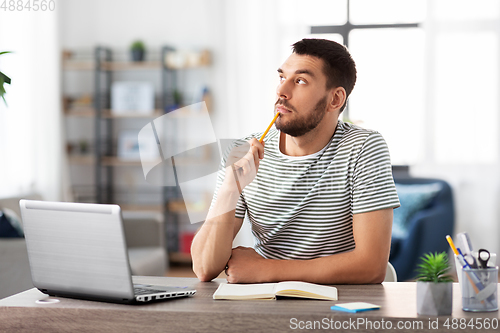 Image of man with notebook and laptop at home office