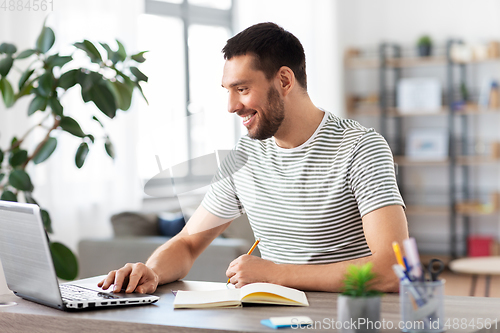 Image of man with notebook and laptop at home office