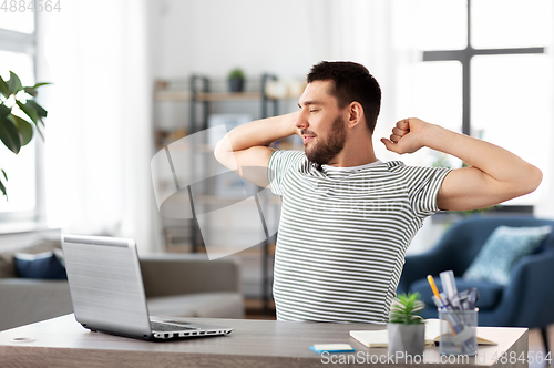 Image of happy man with laptop stretching at home office
