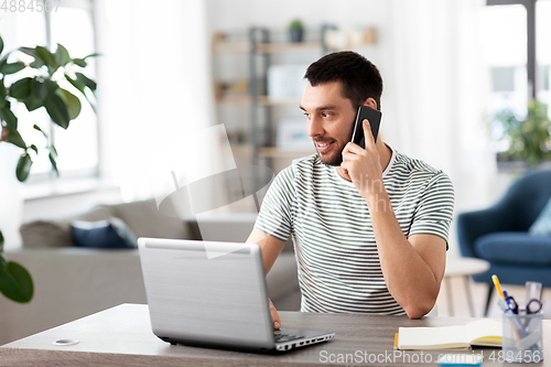 Image of man with laptop calling on phone at home office