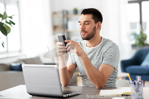 Image of man with smartphone and laptop at home office