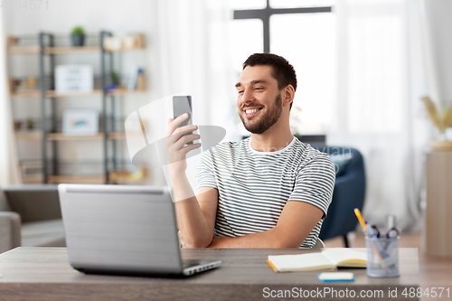 Image of man with smartphone and laptop at home office