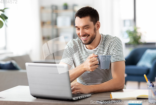 Image of man with laptop drinking coffee at home office