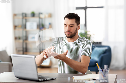 Image of man using hand sanitizer at home office