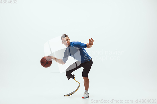 Image of Athlete with disabilities or amputee isolated on white studio background. Professional male basketball player with leg prosthesis training and practicing in studio.