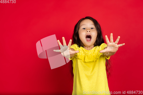 Image of Beautiful emotional little girl isolated on red background. Half-lenght portrait of happy child gesturing