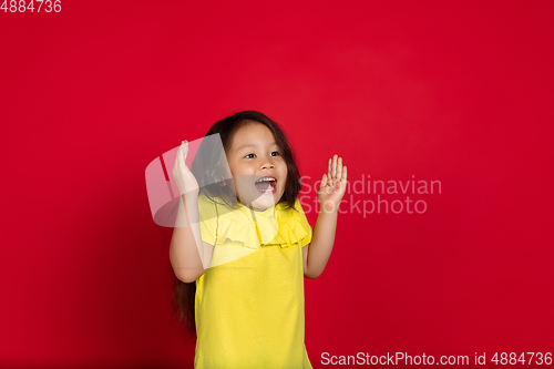 Image of Beautiful emotional little girl isolated on red background. Half-lenght portrait of happy child gesturing