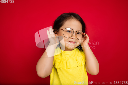 Image of Beautiful emotional little girl isolated on red background. Half-lenght portrait of happy child gesturing