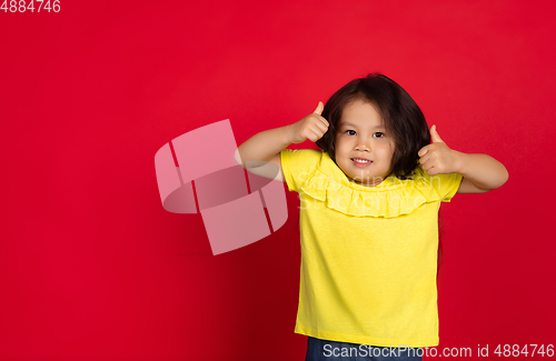 Image of Beautiful emotional little girl isolated on red background. Half-lenght portrait of happy child gesturing