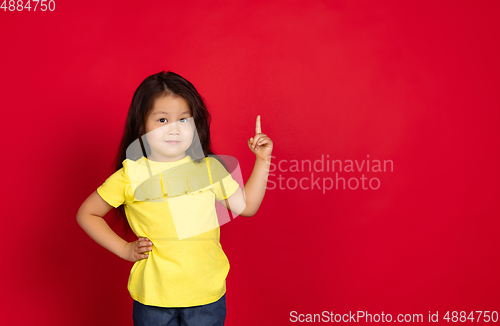 Image of Beautiful emotional little girl isolated on red background. Half-lenght portrait of happy child gesturing