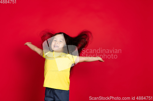 Image of Beautiful emotional little girl isolated on red background. Half-lenght portrait of happy child gesturing